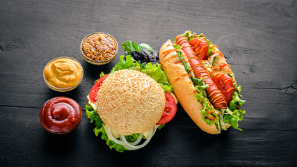 Hot dog and hamburger with cheese, meat and greens on Wooden background. Top view. Free space.