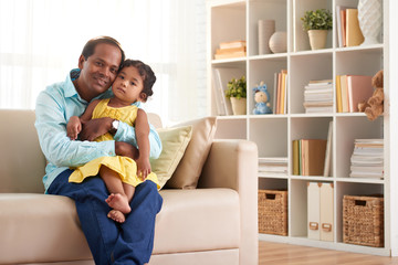 Portrait of loving Indian father hugging his pretty little girl and posing for photography  in cozy living room