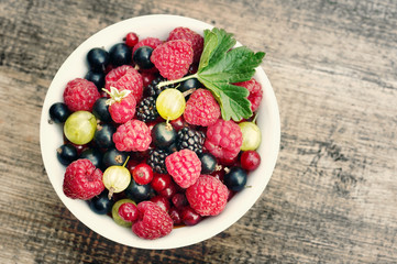 Juicy berries raspberries, currants, blackberries, a gooseberry in an white plate on a wooden surface, top view, close up