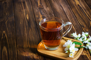 A cup of tea with jasmine flowers on brown wooden background