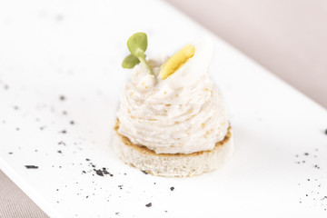 Fresh appetizer with roe salad, on toasted bread, decorated with lemon sliced and green leaf, placed on white plate, light background, isolated