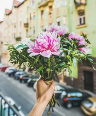 Bouquet of pink and white peony flowers in woman's hand, street background. Flower greeting card concept