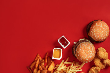 Fast food dish top view. Meat burger, potato chips and nuggets on red background. Takeaway...