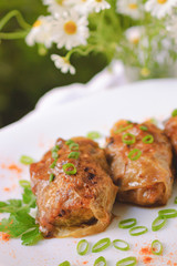 Rustic dinner with stuffed with vegetables cabbage leaves in tomato sauce, Russian dish. The plate stands on the edge of the table, a bouquet of chamomiles in the background. Selective focus