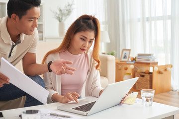 Portrait of young Asian couple using laptop at home while planning new house