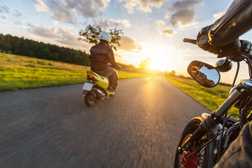 Naklejka premium Motocykliści jadący w kierunku pięknego światła zachodzącego słońca na pustej asfaltowej autostradzie.