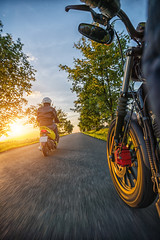 Motorbike riders driving towards beautiful sunset light on empty asphalt motorway.