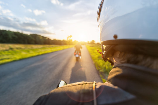 Motorbike riders driving towards beautiful sunset light on empty asphalt motorway.