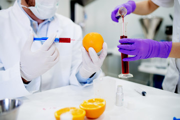 Fototapeta premium Doctor and his assistant doing GMO experiments in laboratory. Injecting chemical substances into orange.