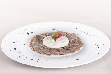 Beef carpaccio with mayonnaise, decorated with herbs, placed on white plate, light background, isolated