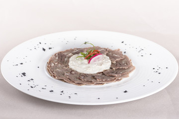 Beef carpaccio with mayonnaise, decorated with herbs, placed on white plate, light background,...