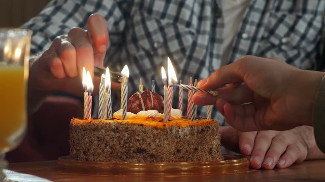 Two hand lighting candles in birthday cake