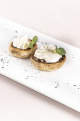 Fresh appetizer with mushrooms, filled with mayonnaise, decorated with green leaf, placed on white plate, light background, isolated