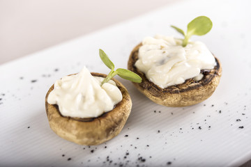 Fresh appetizer with mushrooms, filled with mayonnaise, decorated with green leaf, placed on white plate, light background, isolated