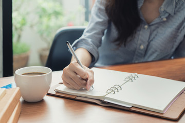 Close-up of young beautiful woman writing in notebook while sitting in chair in front of window at...