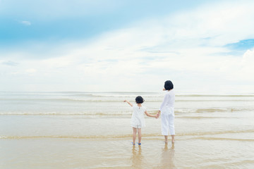 Fototapeta na wymiar Happy Asian family mother and daughter standing on beach looking and point something in sea. Happy family summer vacation concept.