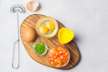  Ingredients for egg mini frittatas on wooden board - tomatoes, scallions, eggs. Top view.