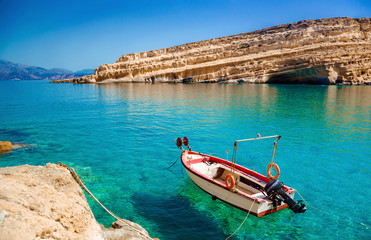 Fototapeta premium Matala beach, old fishing boat and caves on the rocks that were used as a roman cemetery and at the decade of 70's were living hippies from all over the world, Crete, Greece. Rock festival.