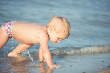 Baby playing on the sandy beach and in sea water. Cute little kid with toys on sand tropical beach. Ocean coast.