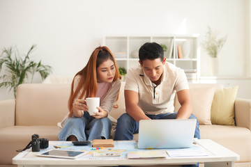 Portrait of young Asian couple booking hotel online while planning vacation for summer