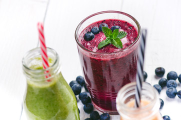 Blueberry, spinachy and orange smoothie on a wooden white background. Glasses of smoothie with berry and mint. Berry, leaf and lime, raspberries on a table. Fruit Healthy food. Breakfast.