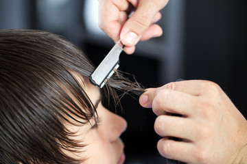 Cutting hair of a young boy with dark hair razor by a hairdresser man and styling hair