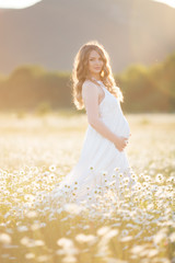 Fototapeta na wymiar Beautiful pregnant woman on the camomile field