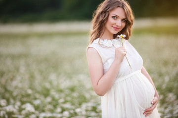 Fototapeta na wymiar Beautiful pregnant woman on the field of daisy flowers