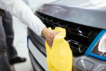 A man cleaning car with microfiber cloth, car detailing (or valeting) concept. Front lights protected with isolation blue tape. Selective focus. 