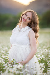 Fototapeta na wymiar Beautiful happy pregnant girl on the field of daisy flowers
