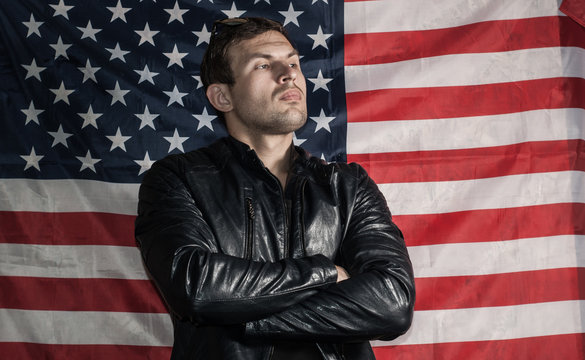 Tough Guy In A Leather Jacket Against The Background Of The American Flag