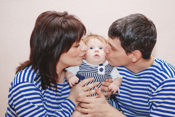 Happy young family dressed identically in tank tops kiss of a child.