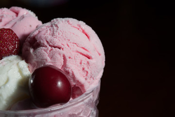 Balls of strawberry, cherry and vanilla ice cream in a glass vase, with fresh berries on a dark background