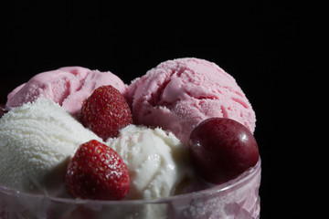Balls of strawberry, cherry and vanilla ice cream in a glass vase, with fresh berries on a dark background