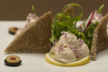 Fish roe salad, whit toasted bread, onion, green leafs, lemon, radish and olives, placed on a white plate, brown background