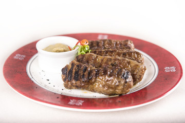 Mici, traditional romanian meat rolls, served with mustard, decorated with green and red leafs, placed on a white and red plate, light background