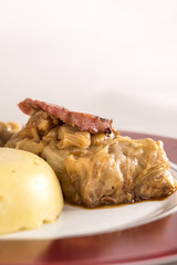 Sarmale, a traditional Romanian stuffed cabbage dish, served with polenta, bacon and hot chilli, placed on a white and red plate, light background