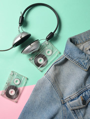 Jeans jacket, audio cassettes, headphones are lined on a blue pink pastel surface. Fashion 80s. Fashionable look. Flat lay.

