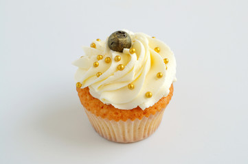 Cupcake with white cream, blueberry and gold confectionery sprinkling. Picture for a menu or a confectionery catalog.