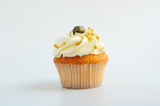 Cupcake with white cream, blueberry and gold confectionery sprinkling. Picture for a menu or a confectionery catalog.