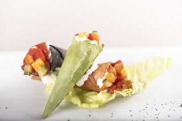 Fresh appetizer with colored pastry cones, filled with cream cheese and vegetables, decorated with green leaf, placed on green salad, white plate, light background, isolated