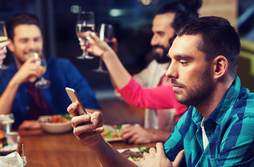 man with smartphone and friends at restaurant