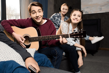 boy playing acustic guitar while his friends listening at home, teenagers playing guitar concept