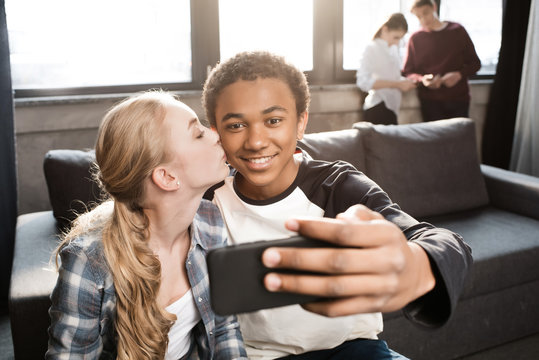 Happy teenage couple taking selfie with friends standing behind, teenagers having fun concept