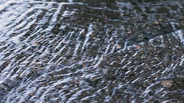 Stream of puddle of rain on a street. Close up flowing water on asphalt road after rainfall
