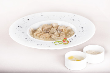 Tripe soup, served with garlic sauce – “mujdei” and horseradish sauce, decorated with green and red leafs, placed on white plate, light background, isolated
