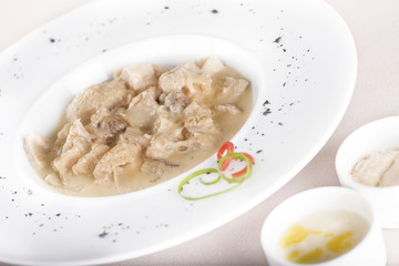 Tripe soup, served with garlic sauce – “mujdei” and horseradish sauce, decorated with green and red leafs, placed on white plate, light background, isolated
