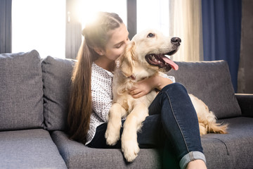 teenager girl hugging golden retriever dog on sofa at home