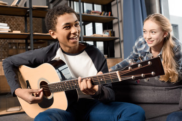african american boy playing acustic guitar while girl listening at home, teenagers playing guitar concept