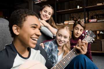 african american boy playing acustic guitar while his friends listening at home, teenagers playing guitar concept